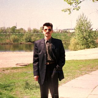 Man standing outdoors near lake by paved path.