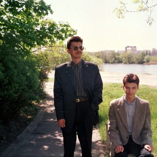 Two men posing by a riverbank in springtime.