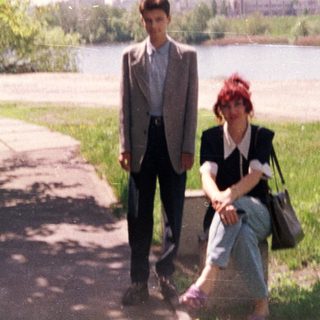 Two people walking and sitting by a river.