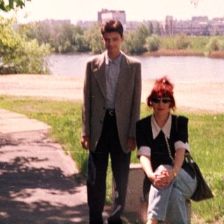 Two people walking by a riverbank in springtime.