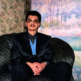 Man in formal attire sitting on armchair.
