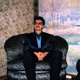 Man in formal attire sitting in armchair indoors.