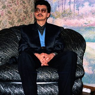 Man in formal attire sitting in armchair indoors.