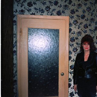 Woman standing between two closed doors in dimly lit floral-patterned hallway.