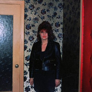 Woman standing between two closed doors in dimly lit floral-patterned hallway.