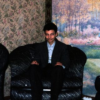Man sitting on velvet armchair indoors near landscape mural.