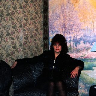 Woman sitting in dimly lit room with sunset mural.