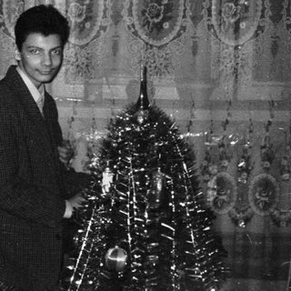 Elegant couple posing near festive Christmas tree in ornate hall.