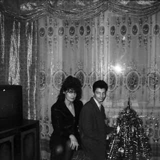 Elegant couple posing near festive Christmas tree in ornate hall.