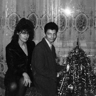 Elegant couple posing near festive Christmas tree in ornate hall.