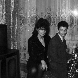 Elegant couple posing near festive Christmas tree in ornate hall.