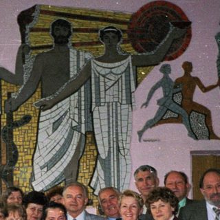 Group posing indoors near mural depicting industrial and agricultural scenes.