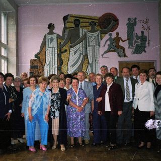 Group posing indoors near mural depicting industrial and agricultural scenes.