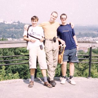 Three people posing on an elevated viewpoint overlooking a city.