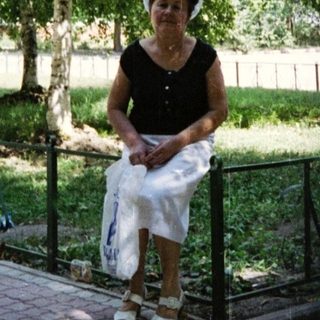 Woman in white dress and hat holding bag outdoors.