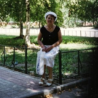 Woman in white dress and hat holding bag outdoors.