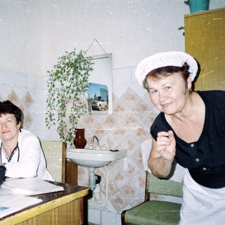 Two women sitting indoors, one writing, the other posing.