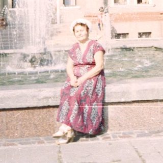 A woman sits near a fountain in front of a large building.