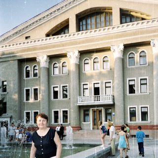 Woman posing near fountain in front of grand building.