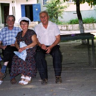 Five adults posing together outdoors near a building.
