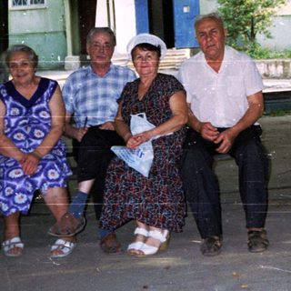 Five adults posing together outdoors near a building.
