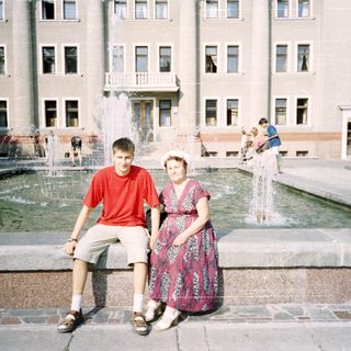 Two people posing by a fountain in front of a building.