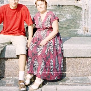 Two people posing by a fountain in front of a building.