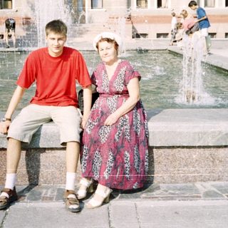 Two people posing by a fountain in front of a building.