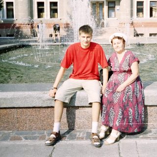 Two people posing by a fountain in front of a building.
