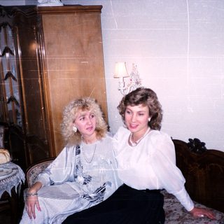 Two women posing together indoors in vintage-style room.