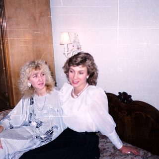 Two women posing together indoors in vintage-style room.