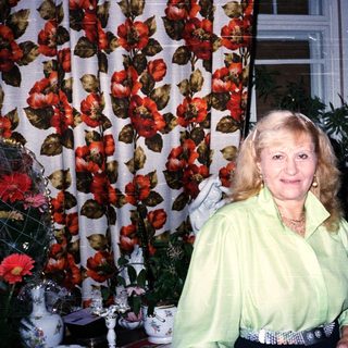Woman in green blouse posing indoors near floral curtain.