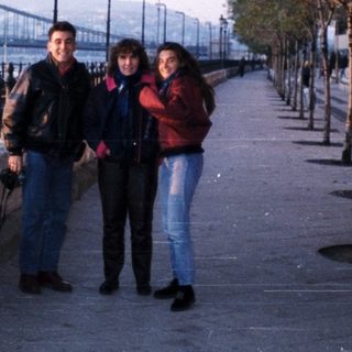 People walking along riverside promenade near bridge.