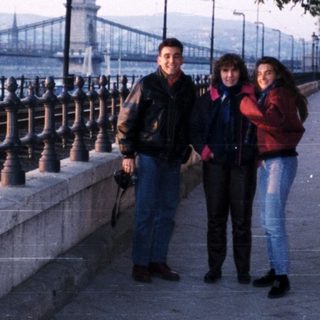 People walking along riverside promenade near bridge.