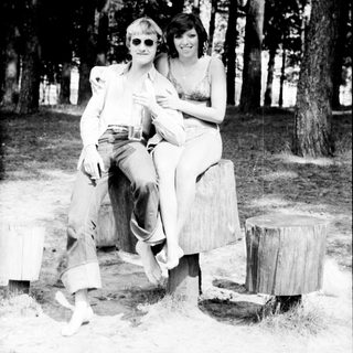 Two people posing together outdoors on stumps.