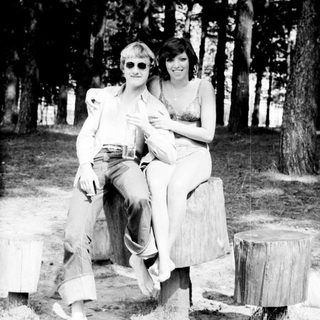 Two people posing together outdoors on stumps.