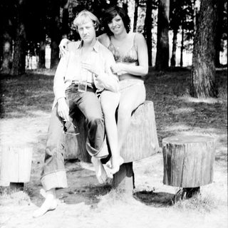 Two people posing together outdoors on tree stumps.