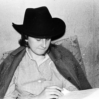 Person wearing cowboy hat writing at desk.
