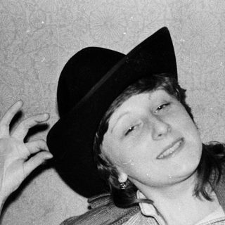 Young person reading book while wearing a fedora.