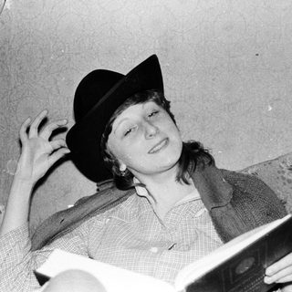 Young person reading book while wearing a fedora.