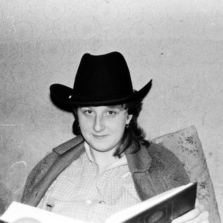 Person wearing cowboy hat reading book indoors.