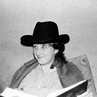 Person wearing cowboy hat reading book indoors.