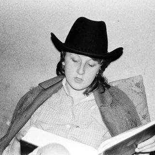 Person wearing cowboy hat reads book indoors.