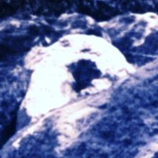 Here's a brief summary of the image: Large rocks emerge from a dark, forested area.