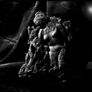 Here's a brief summary: Statue of a figure, possibly male, in a dark setting.
