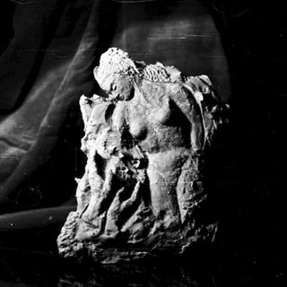 Here's a brief summary of the image: Clay sculpture of a figure on a textured black surface.