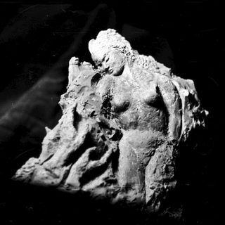 Here's a brief summary of the image: Sculpted figure of a woman, dark background, textured surface.