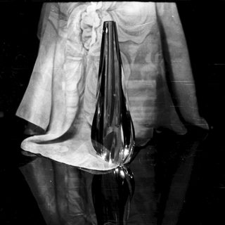 Black vase sits on a draped cloth in shadow.