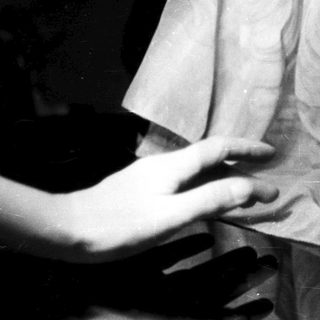 Here's a brief summary of the image: A hand near a glass vase, dark background.