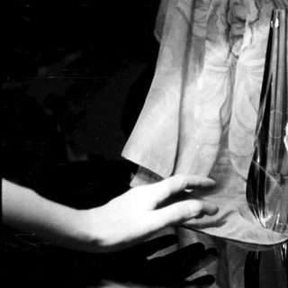 Here's a brief summary of the image: A hand near a glass vase, dark background.